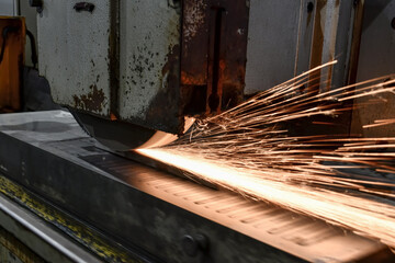 Sparks fly from the abrasive wheel when grinding and finishing metal on a surface grinder.