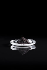 Caviar negro de esturión sobre una piedra de hielo reflejada en fondo negro. Comida delicatessen de lujo	