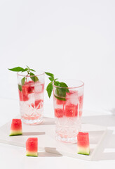 Dos vasos de jugo de sandía desintoxicante con hojas verdes trozos de sandia y hielo sobre fondo claro	