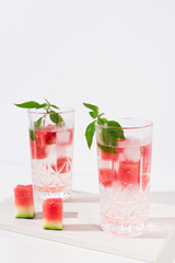 Dos vasos de jugo de sandía desintoxicante con hojas verdes trozos de sandia y hielo sobre fondo claro	