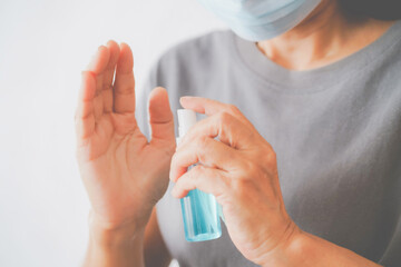 senior woman's hand holding alcohol spray bottle to clean her hand, in soft focus, due to spread of corona virus, population, social or herd immunity concept