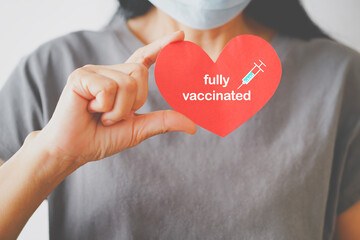 senior woman's hand holding red heart with fully vaccinated text and syringe icon, due to spread of corona virus, population, social or herd immunity concept - obrazy, fototapety, plakaty