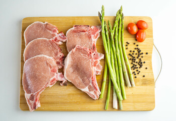 Una tabla de madera con chuletas de cerdo, esparragos y tomates cherry