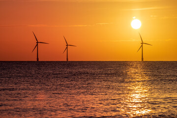 Beautiful orange sunrise with silhouetted offshore wind farm turbines. Clean energy ecotourism and...