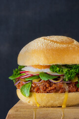 Close-up burger of fresh raw minced pork,vegetables with fried eggs and streaks of yolk,dark backdrop.Traditional yummy German dish with peppered matt and bun,greenery,selective focus,copy space.