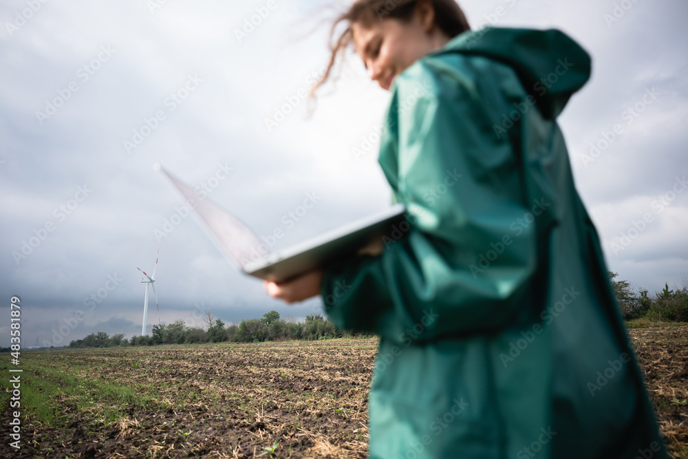 Poster blurred farmer with laptop on the field. focus on wind turbines on a background. sustainable farming