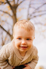 a little boy in a beige knitted jacket in Dad's arms against sky and branches