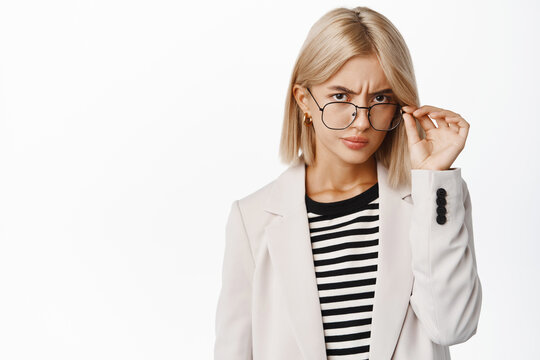 Suspicious young woman looking under glasses, squinting and staring doubtful, having concern, standing over white background