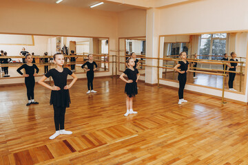 Girls 8 years old in black suits are doing choreography in a ballet class.