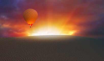 Hot air balloon flying over red desert of sand dune at sunset
