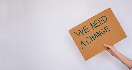 Hand holding cardboard with 'we need a change' inscription.