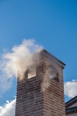 historical brick chimney on the roof with a steaming smoke