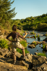 An asian female fly fisher women wearing waders, resting a rod on her shoulder