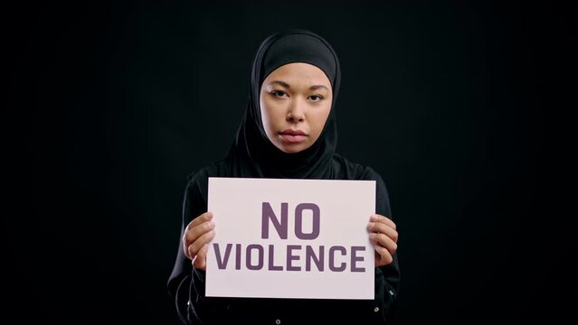 Muslim young woman in hijab holding no violence sign, women's rights protection