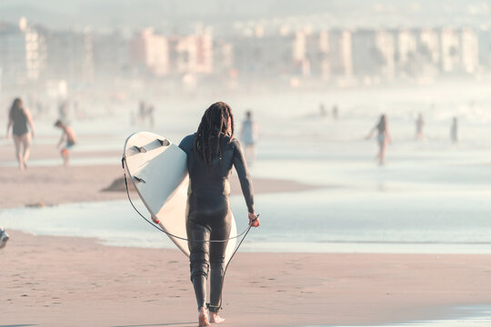 young latin surfer walking on the beach of La Serena at sunset, back view