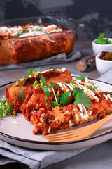 Enchiladas with crepes, chicken meat, tomato sauce and cheese served with sour cream and herbs served on the plate. Fusion cuisine meal