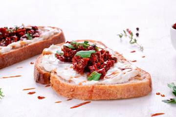 Bruschetta with sun-dried tomatoes and cream cheese on the slice of ciabatta bread garnished with balsamic sauce on the white table. Mediterranean cuisine appetizer