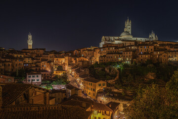 Fototapeta na wymiar Amazing night cityscape with two iconic landmarks: Torre del Mangia on the right and the Cathedral of Siena on the left, Tuscany, Italy