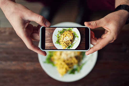 Man takes photo of spaghetti meal in restaurant using smartphone. Food photography with smartphone