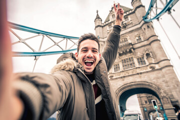 Smiling man taking selfie portrait during travel in London, England - Young tourist male taking holiday pic with iconic england landmark - Happy people wandering around Europe concept - obrazy, fototapety, plakaty