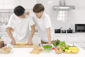 Young asian male LGBT couple happy spending time together during cooking bread salad in white kitchen with smiling face. Selective focus.