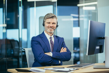 Portrait of senior and experienced businessman with headset for video communication, happy man smiling and looking at camera, man at work