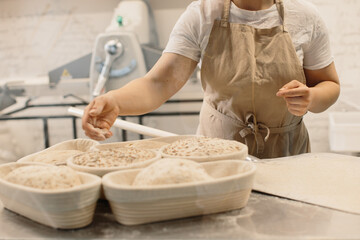 Baker woman sprinkles flour on the shaped loaves, rustic style, bread before baking, rustic whole grain bread.