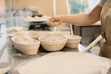 Baker woman sprinkles flour on the shaped loaves, rustic style, bread before baking, rustic whole grain bread.