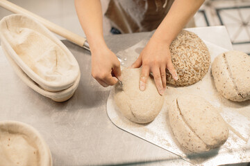 women's hands make an incision on a round dough before baking bread.