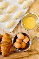 Croissant baking concept. Raw rolled up and freshly baked croissants as well as ingredients lie on the table.