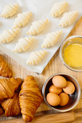 Croissant baking concept. Raw rolled up and freshly baked croissants as well as ingredients lie on...