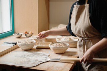 The baker sprinkles flour on the raw bread lying on the peel.