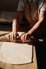 Woman hands rolling out dough in flour with rolling pin in bakery.