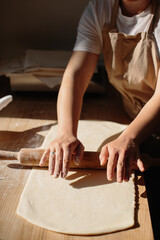 Woman hands rolling out dough in flour with rolling pin in bakery.