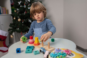 Beautiful toddler play with a wooden toys at home. Toddler play with a color educational toy and wooden car.  Child play at the table in the baby room near Christmas tree.  Funny baby. Lifestyle. 