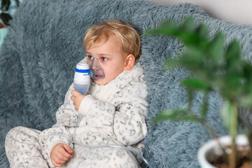 Cute baby boy makes inhalation with a nebulizer equipment. Sick child holding inhalator in hand and...