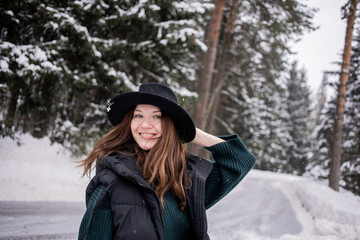 Caucasian young woman in black hat in winter snowy forest.