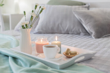 Fototapeta na wymiar cup of coffee on wooden tray on bed with flowers and candles