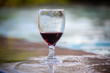 Glass of red wine standing at the edge of the swimming pool