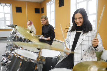 Young adult men and women learn to play drums at school. Hobbies and pastime.
