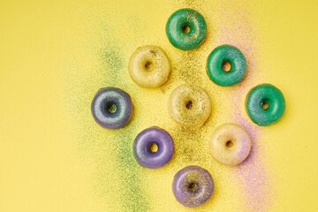 Mardi Gras donuts with traditional color topping on yellow background.