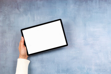 Woman hand holding digital tablet computer with blank white screen mock up on gray color background. Top view, copy space