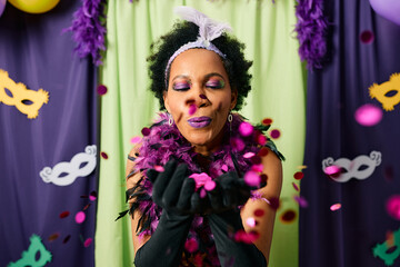 Black woman blows confetti and has fun on Mardi Gras carnival party.