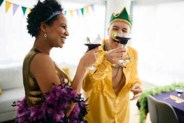 Happy African American woman and her Caucasian friend wear Mardi Gras costumes while toasting...