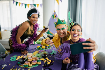 Multiracial friends in carnival costumes have fun while taking selfie and celebrating Mardi Gras at...