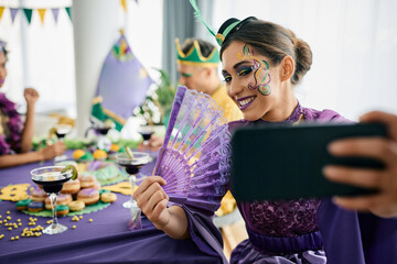 Young woman in Mardi Gras costume taking selfie during carnival home party.