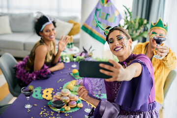 Group of cheerful friends in carnival costumes celebrate Mardi Gras and take selfie with smart phone. - obrazy, fototapety, plakaty