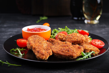 Chicken nuggets and sauce in black plate on a dark background.