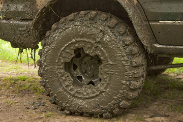 Fototapeta na wymiar Dirty offroader wheel is standing on the road with the ground. Jeep after an off-road trip.
