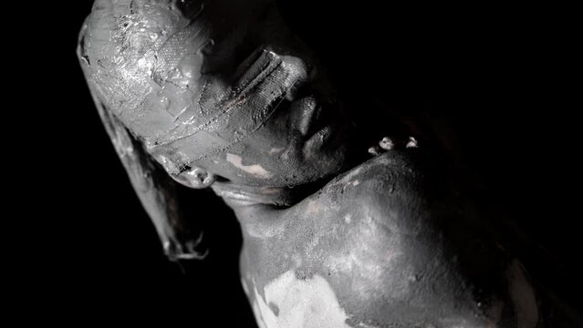 live clay statue of blindfolded woman is moving in darkness, smearing mud on body